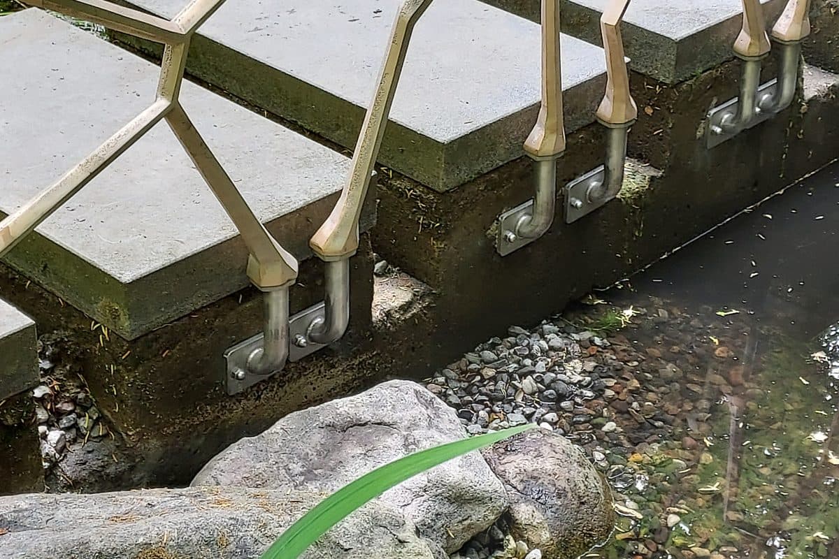 Dasselbe Bronzegeländer nach der Montage: Pfosten auf Edelstahlkonsolen an der Kante eines Gartenteichs