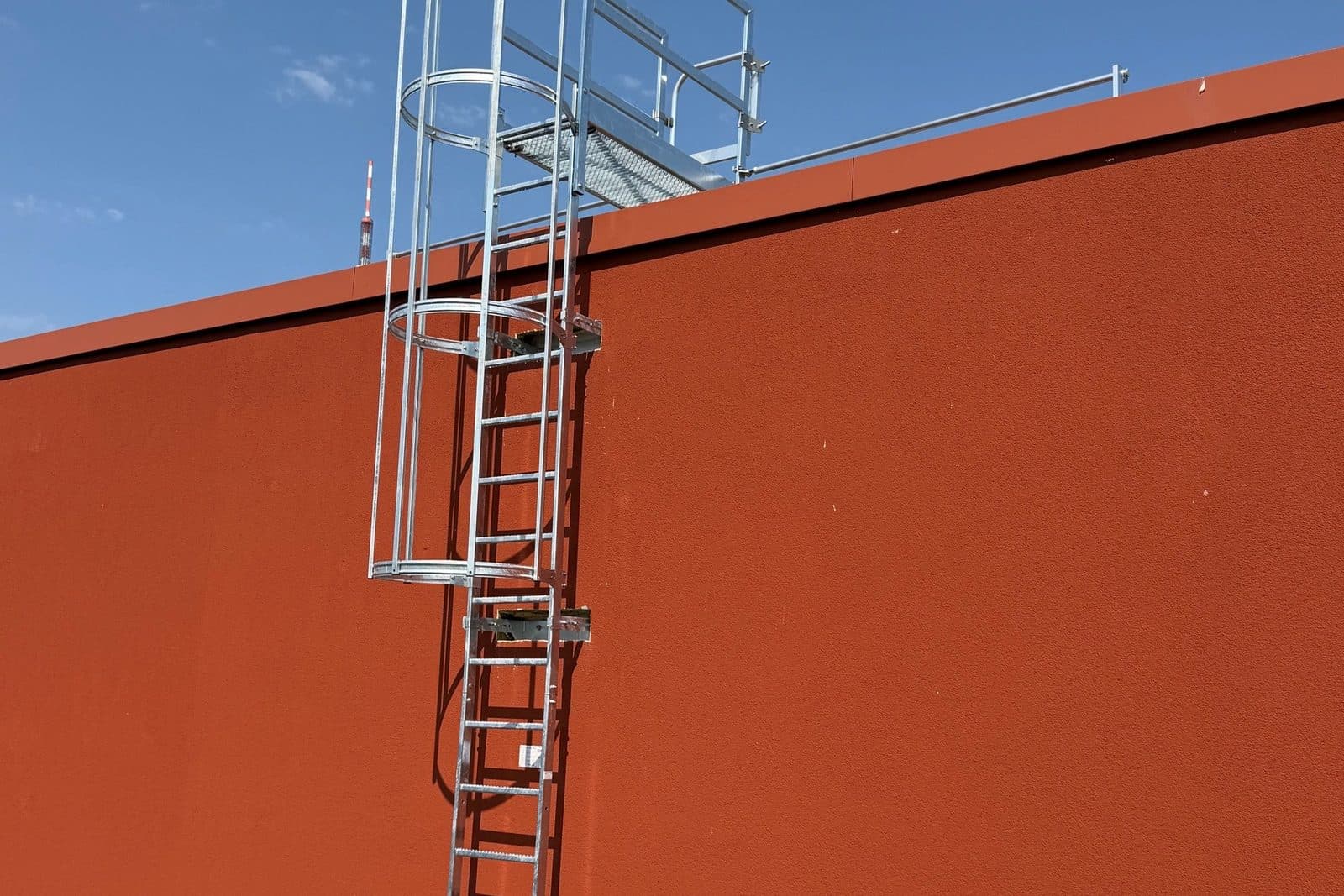 Verzinkte Steigleiter mit Rückenschutz an einer Gebäudefassade