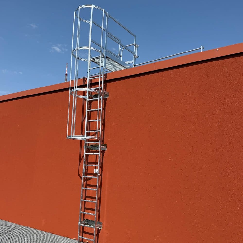 Steigleiter mit Rückenschutzkorb an einer roten Hallenwand